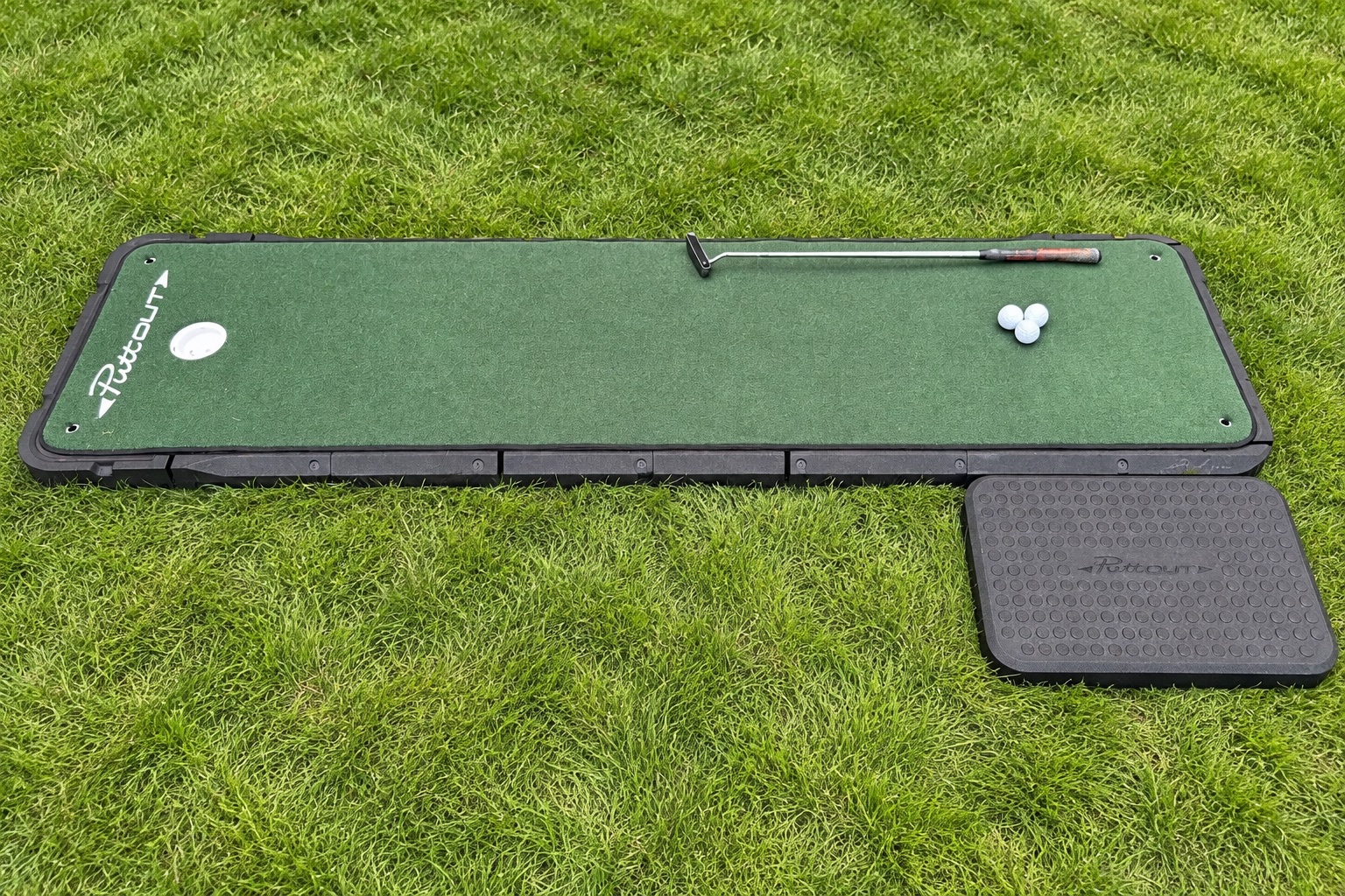 Close view of the putting mat, standing pad, putter, and golf balls
